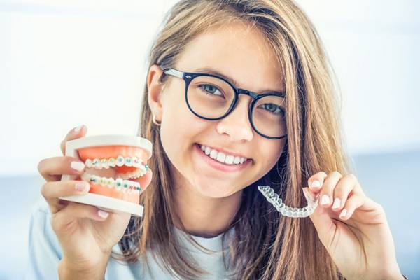 Smiling teen girl holding braces model and clear aligner at SS Orthodontics in Glendale and Phoenix, AZ
