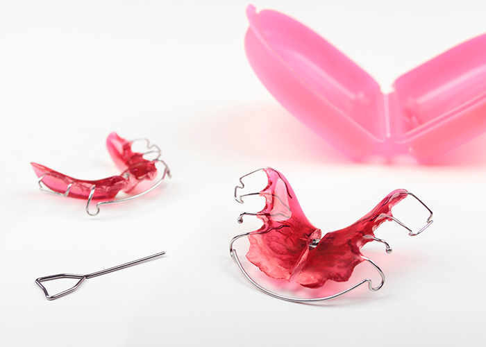 Pink removable retainers with storage case and adjustment key on white background at SS Orthodontics in Glendale and Phoenix, AZ