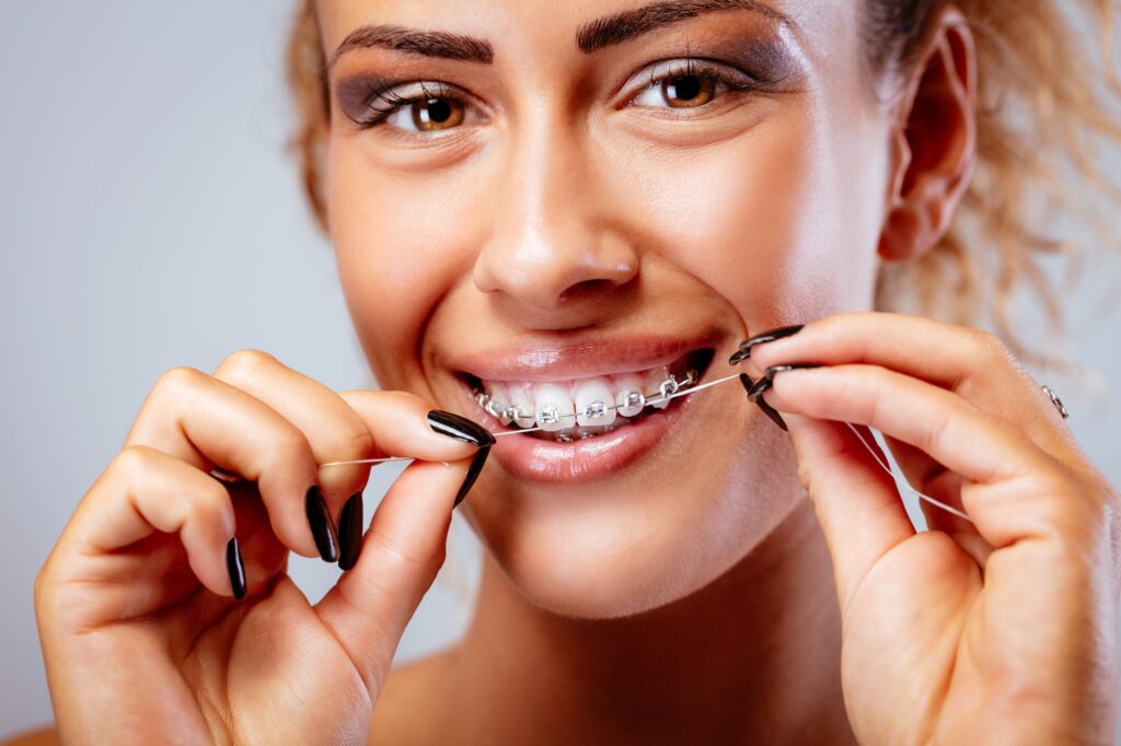 Smiling woman cleaning braces with dental floss during orthodontic care at SS Orthodontics in Phoenix & Glendale, AZ, featured on New Patient Forms page.
