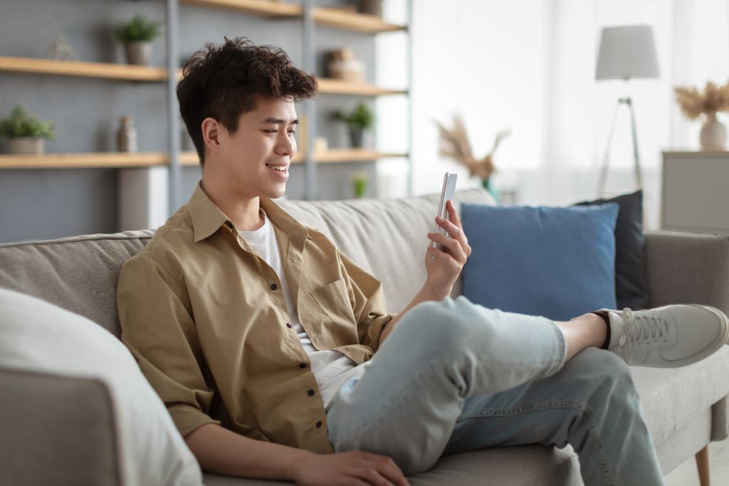 smiling-asian-man-using-smartphone-at-home-sitting
